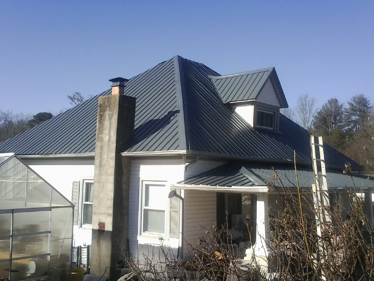 Dark blue standing seam metal roof on a white farmhouse with dormer — Slate & Tile Roof Repair by Roofing Brothers in Shirley