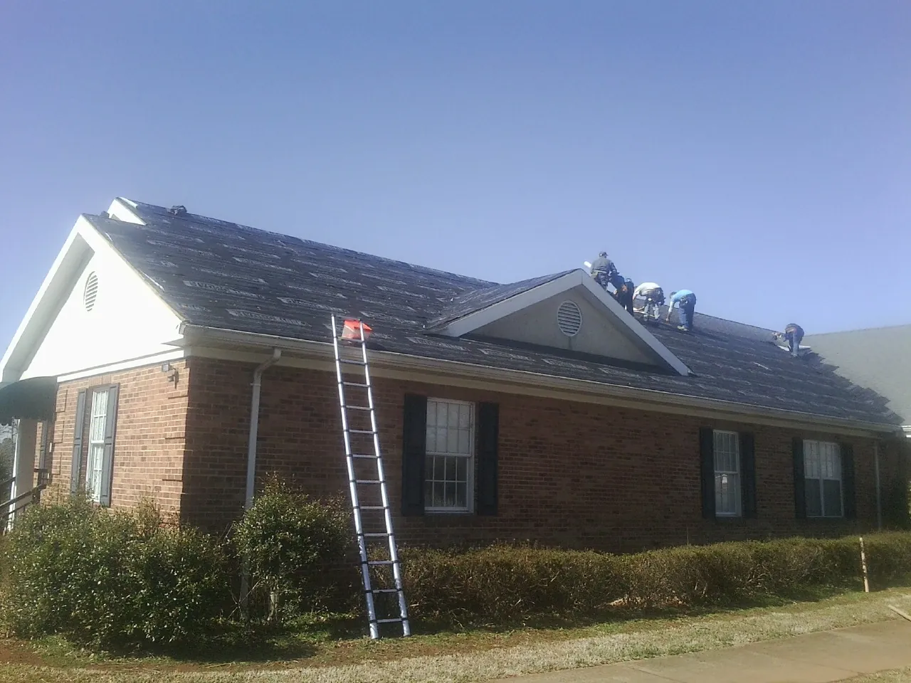 Crew tearing shingles off a brick ranch roof with a ladder set — Emergency Roof Repair work by our crew in Shirley